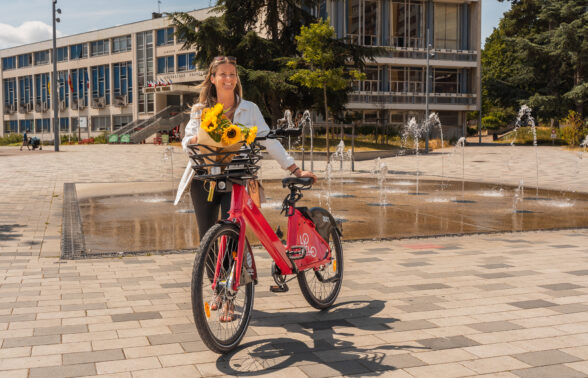 Une femme marche a côté de son Lovélo avec un bouquet de tournesol sur la place de l'Hôtel de ville